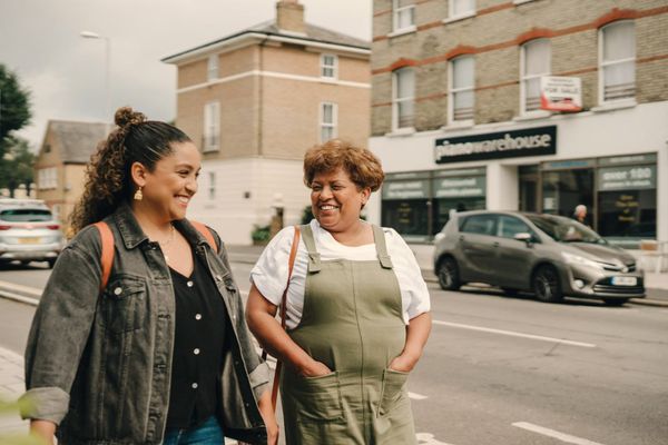 Two women walking down a town street together, chatting and smiling