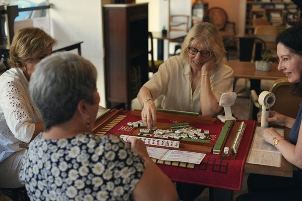 Four older women absorbed in a game of mahjong at a cafe table