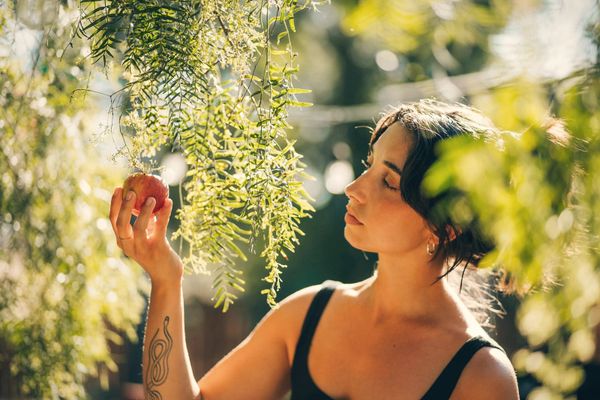 A woman holding an apple under leaves, looking at it
