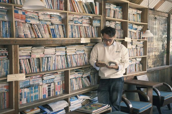 A man standing absorbed in a book in a book-lined second-hand bookshop