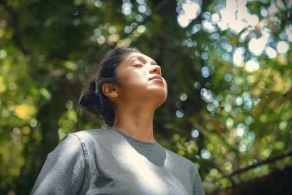 A woman with her face lifted to dappled sunlight, eyes closed, breathing in