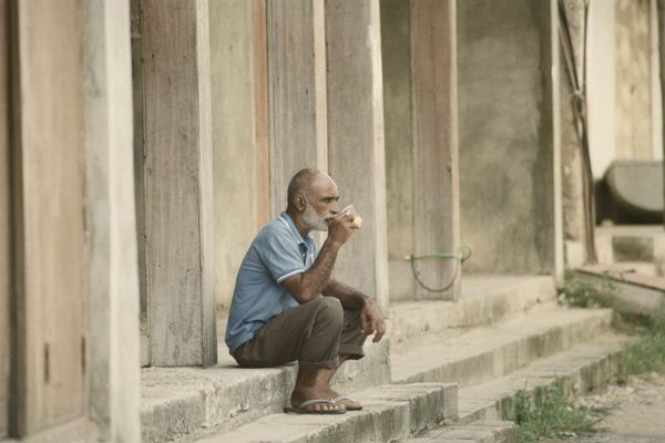 An older man sitting on stone steps, sipping from a small cup