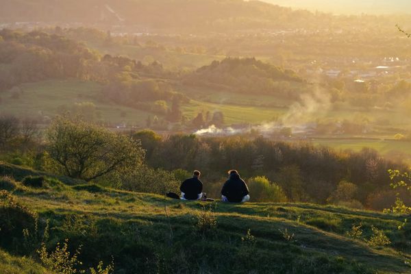 Two friends sitting together on a grassy hillside above a valley in warm autumn haze