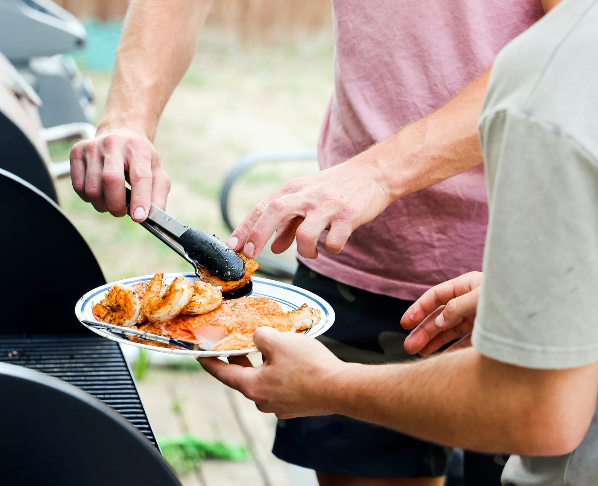 A man serving a friend shrimp and salmon from a grill