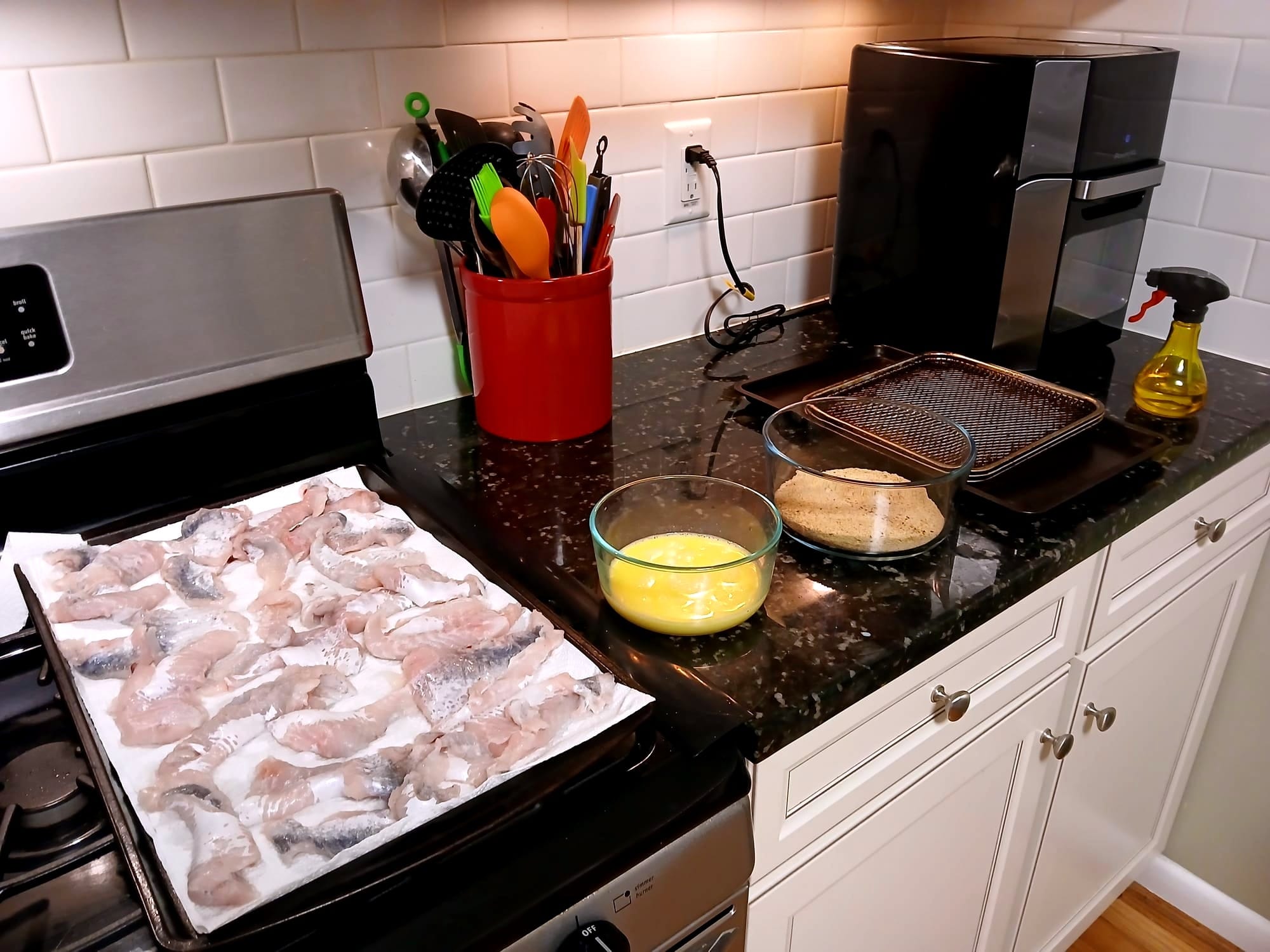 Pieces of fish, egg, breading, and an air fryer with oil