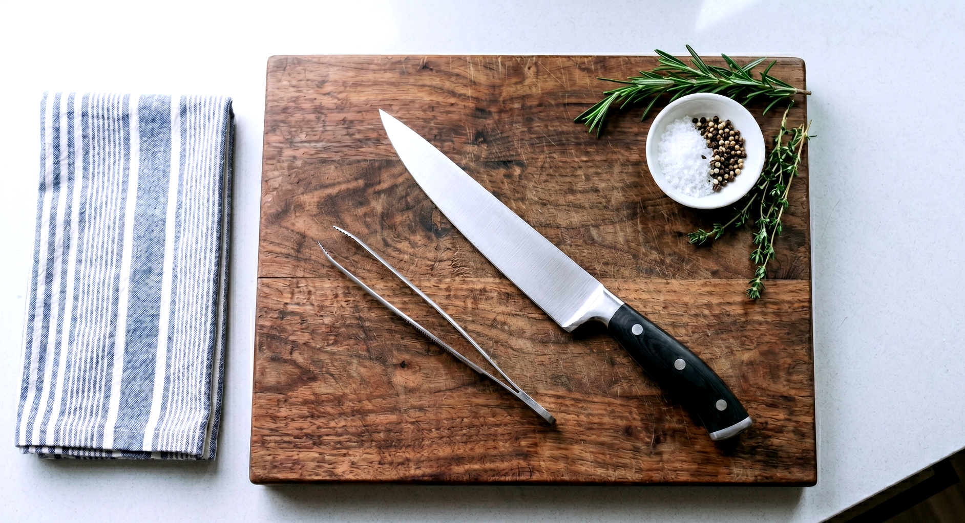 a pristine stainless steel fillet knife, specialized fish tweezers, and a thick wooden cutting board on a clean kitchen counter