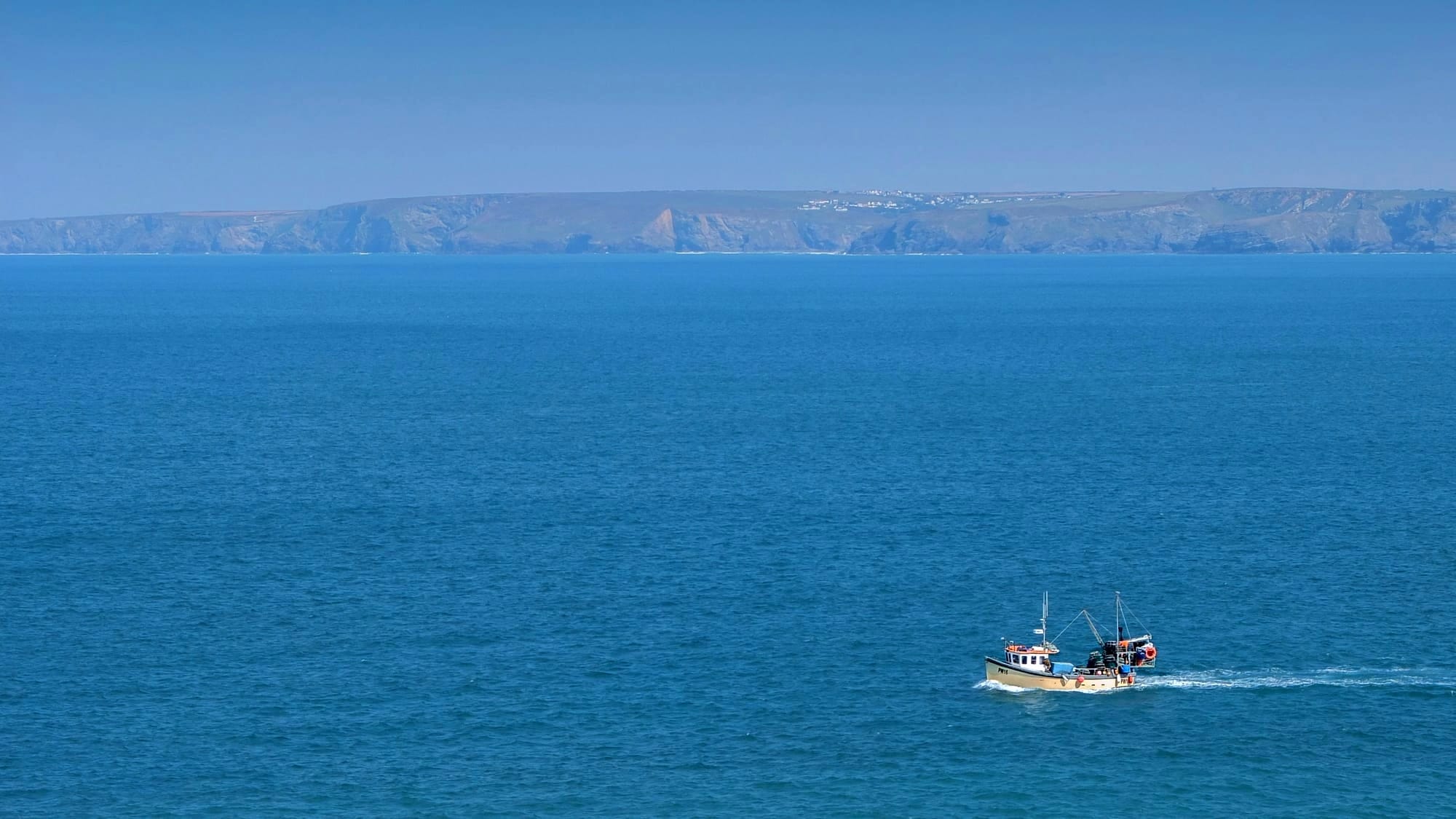 Fishing boat in deep blue open ocean water moving along a coastline