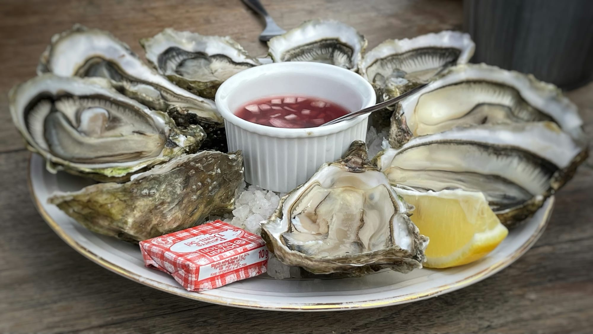 Oysters on the half shell over ice with a wedge of lemon and a ramekin of mignonette on a white plate.