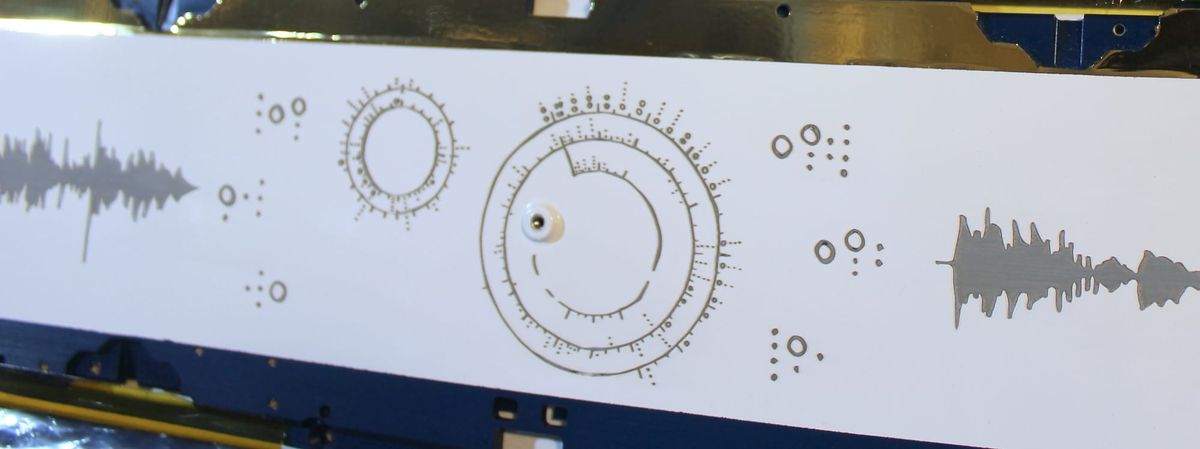 A rectangular aluminum satellite panel, with my circular "iris" notation etched into its white coating, along with chords and audio waveforms.