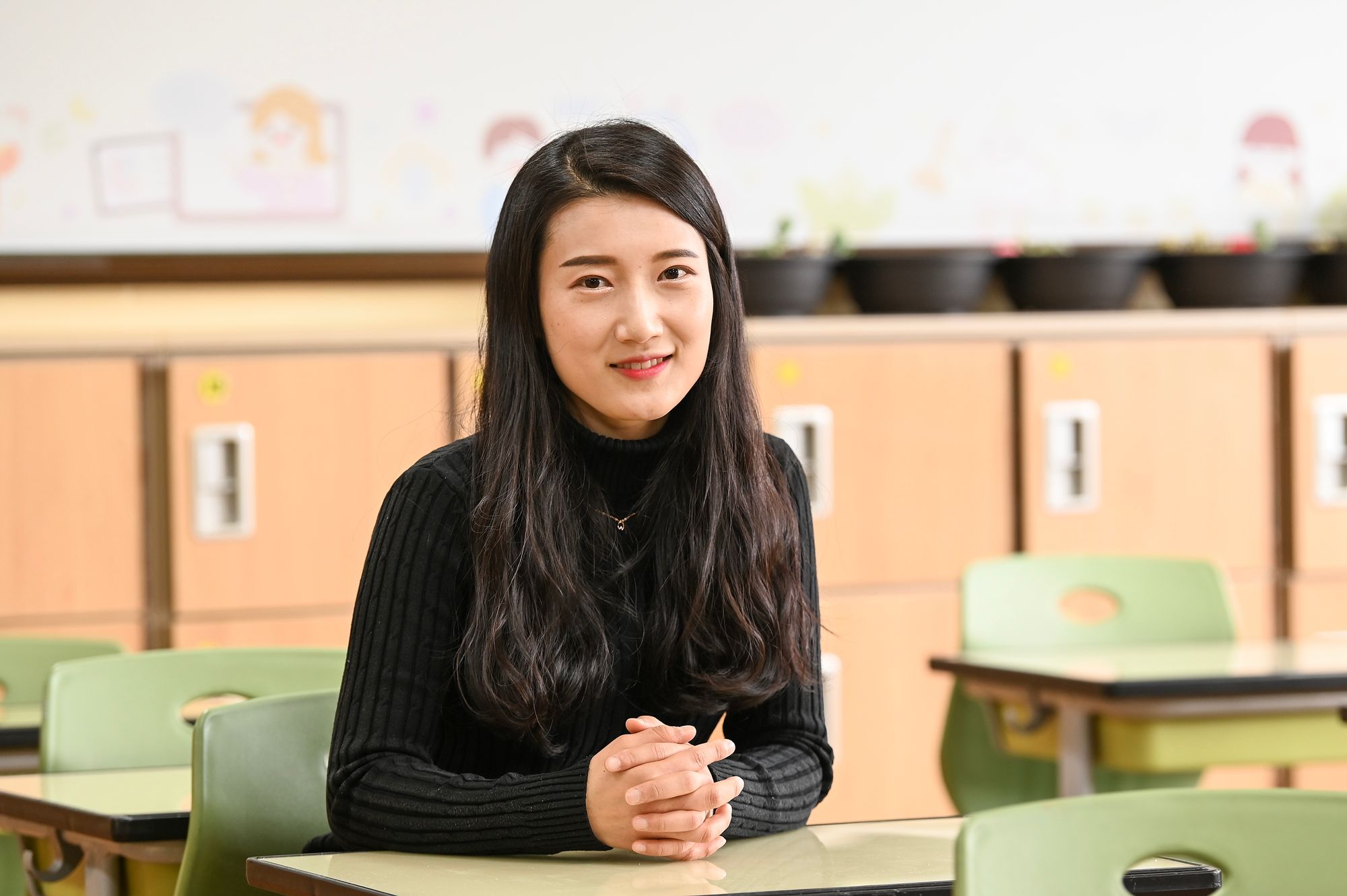 임다정 선생님이 학급 운영의 무대인 교실 안 가운데 앉아 카메라를 보고 미소짓고 있다.