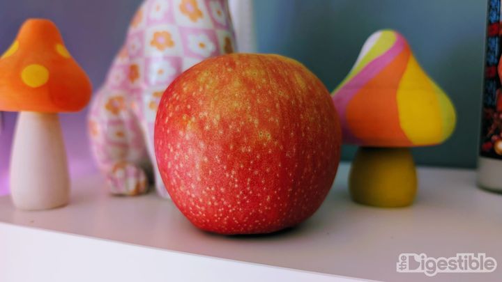 A pink lady apple on a shelf with wooden mushrooms.