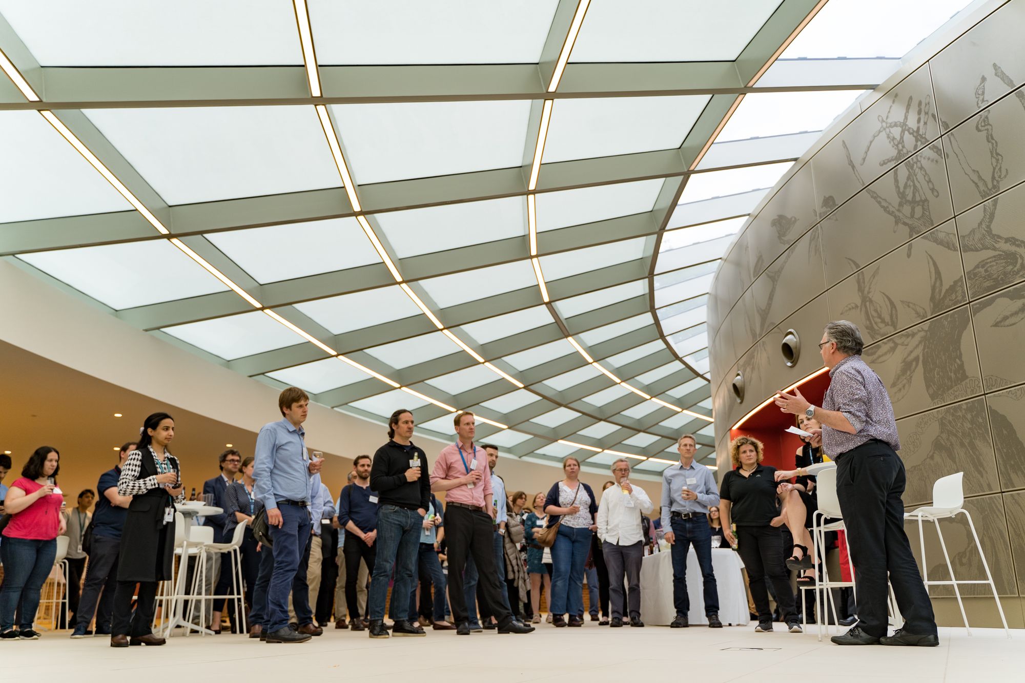 Male person gesturing while giving a speech, facing a group of standing people