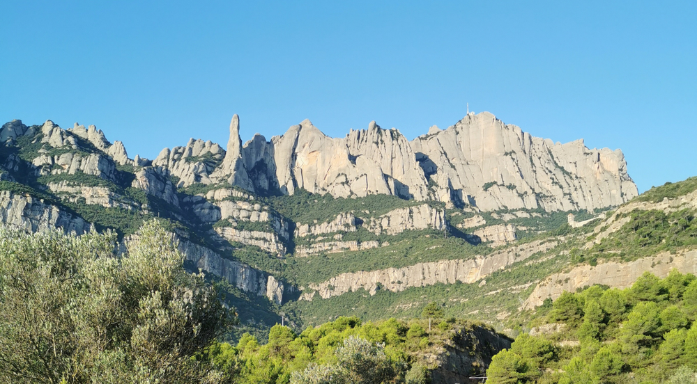 Landscape featuring a bright blue sky, and rocky mountains with streaks of green bushes and tere