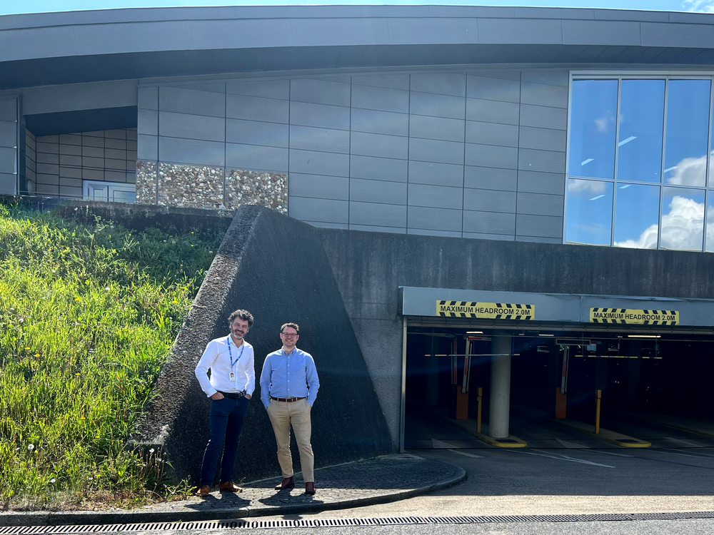 Two men stand in front of the entrance to a car park