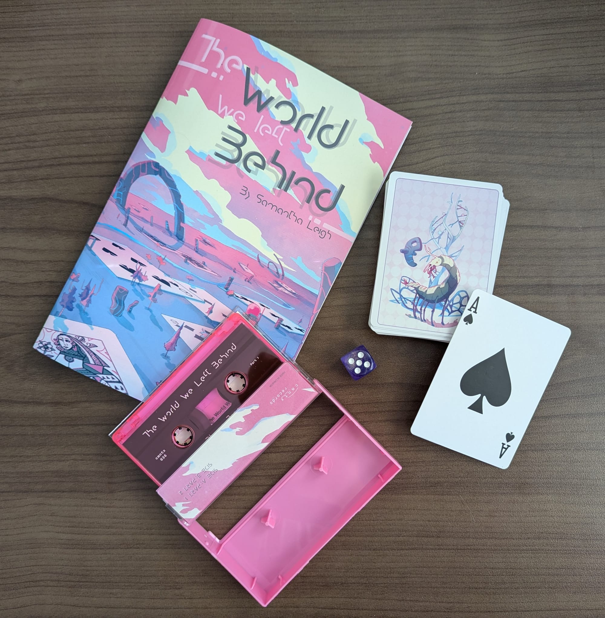 Materials from the box set: a game book, a cassette, a deck of playing cards with art from the game, and a purple die.