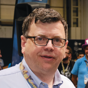 Middle-aged man in glasses set against backdrop of UKGE convention center.