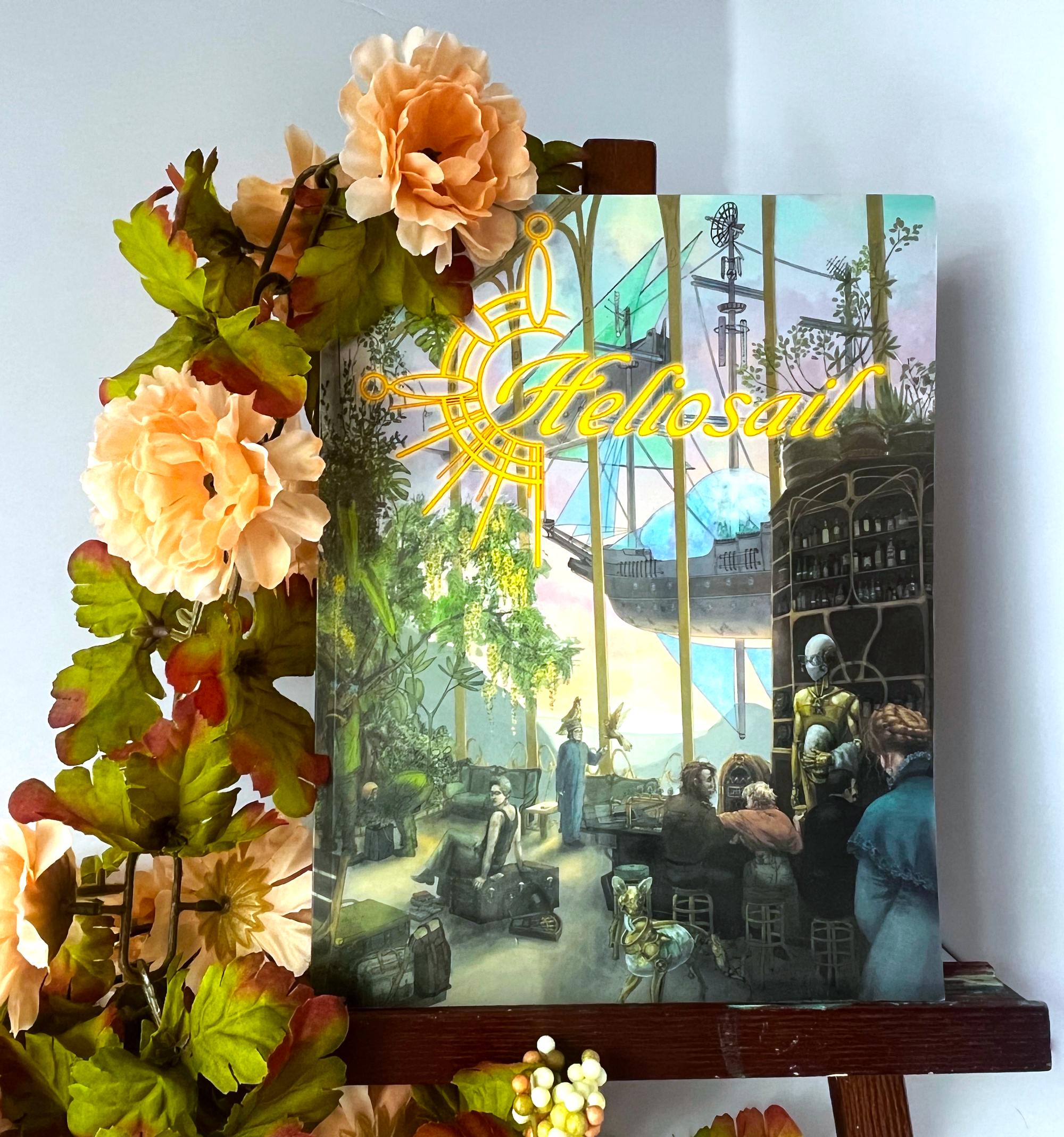 a photograph of the heliosail book on a small easel with soft pink flowers around it.