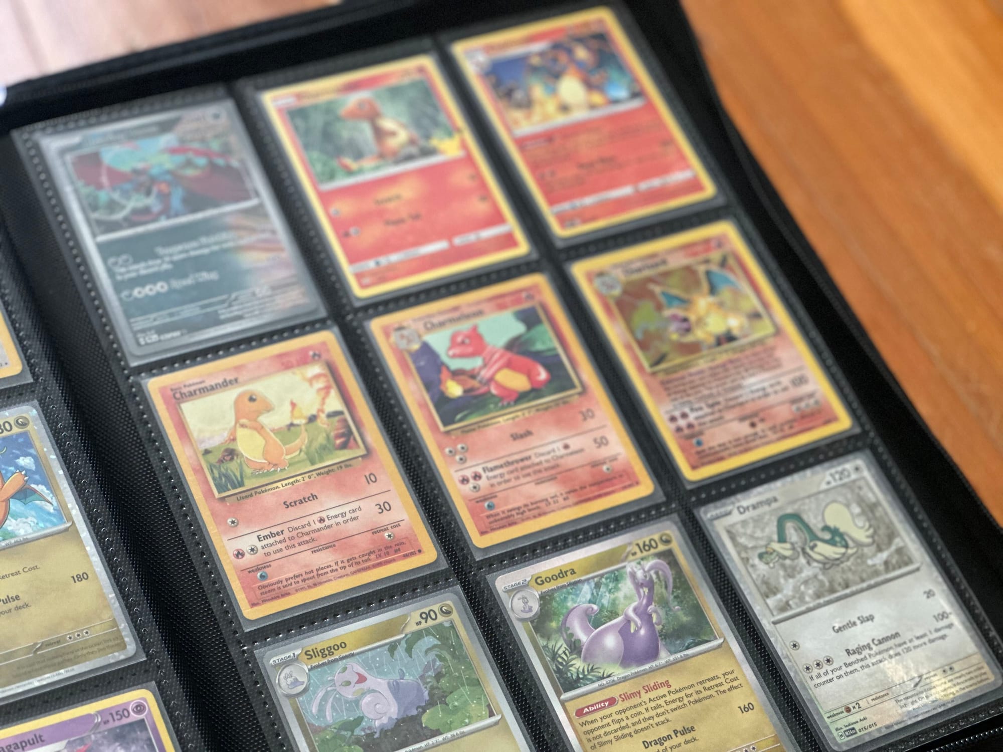 A black binder full of Pokémon cards sitting open on a wooden table.