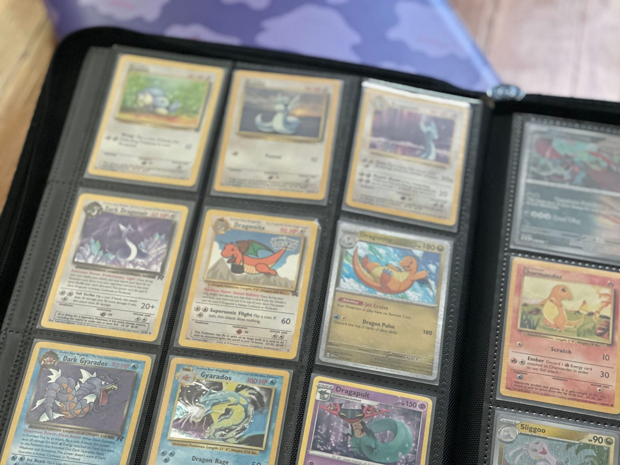 A black binder full of Pokémon cards sitting open on a wooden table.