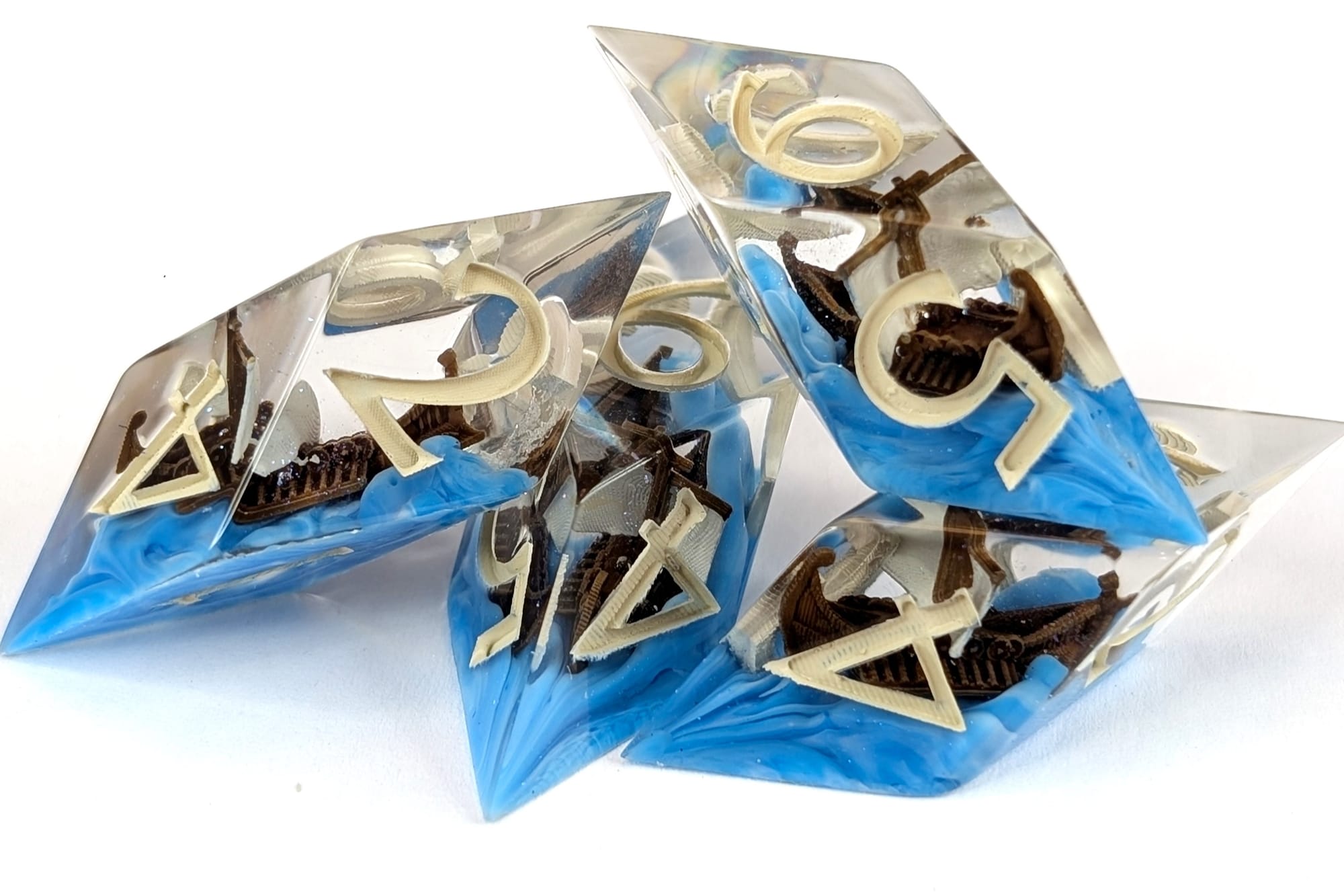 Photograph of Atrapos’ dice. The dice are shard style D6’s. featuring a handpainted miniature 3d model of a greek style ship floating inside.