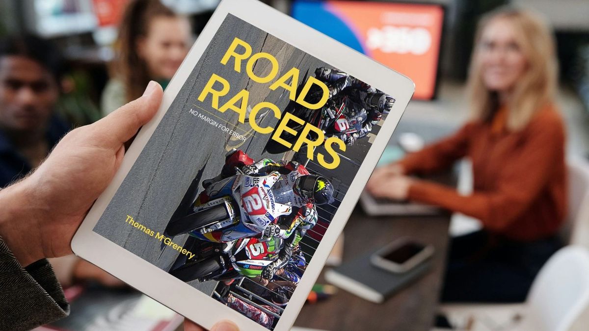 Mockup of Road Racers cover on a tablet being held by someone addressing a group of people seated at a table. 