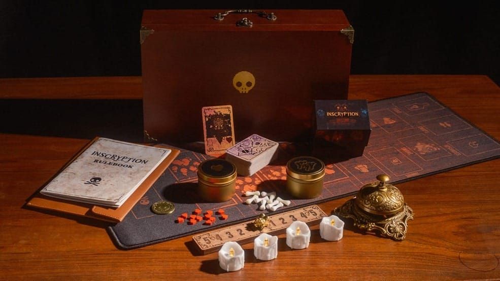 The contents of the Inscryption board game, including the rulebook, cards, playmat, wooden scale, and a brass bell.