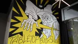 Concrete wall mural of a scowling wizard (black and white) casting a bright yellow spell with downturned hand. Stylized letters read: Tabletop Bookshelf.