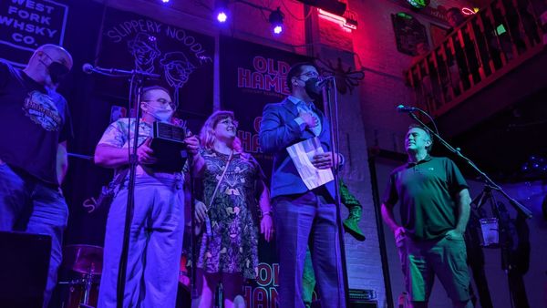 Five people stand on a stage, accepting an award. One in a blue suit gives a speech. Another holds the trophy.