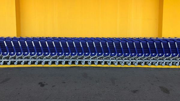 Dozens of blue shopping carts in a horizontal line against a yellow building ediface.