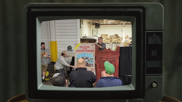 Old TV set framework showing Goodman Games employees revealing the cover of City State of the Invincible Overlord.