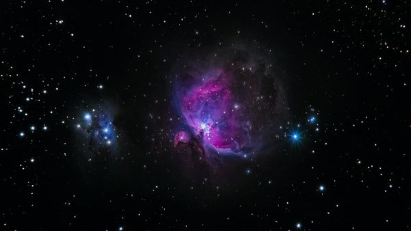 Photograph of a purple and blue nebula, along with hundreds of stars, set against the black of space.