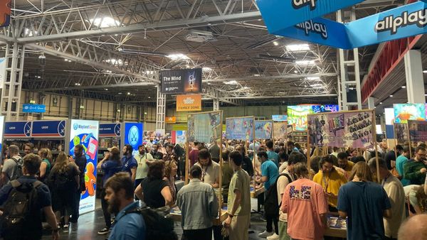 Crowd of UKGE attendees inside the convention center. A blue sign hanging above reads "allplay"