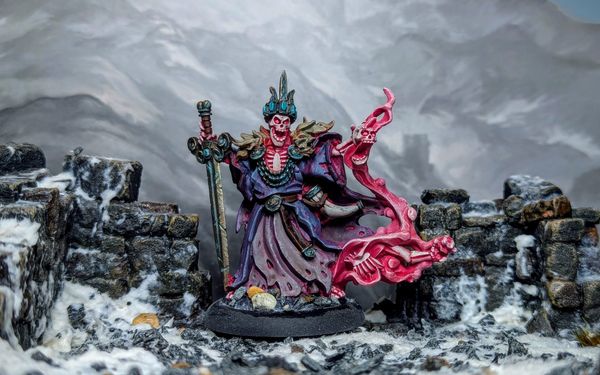 A photo of a miniature skeleton in purple robes, standing amidst ruins against a snowy backdrop.