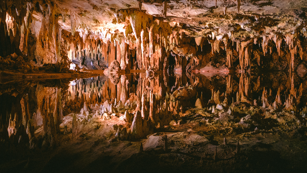 A photograph of an underground lake, the mirror-like surface reflecting the white and orange-colored stalactites, making it difficult to separate ceiling from floor. 