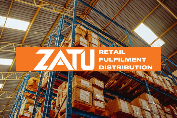Shipping warehouse with cardboard boxes on blue metal shelves. Perspective skewed towards ceiling. Zatu logo, orange on white, overlaid.