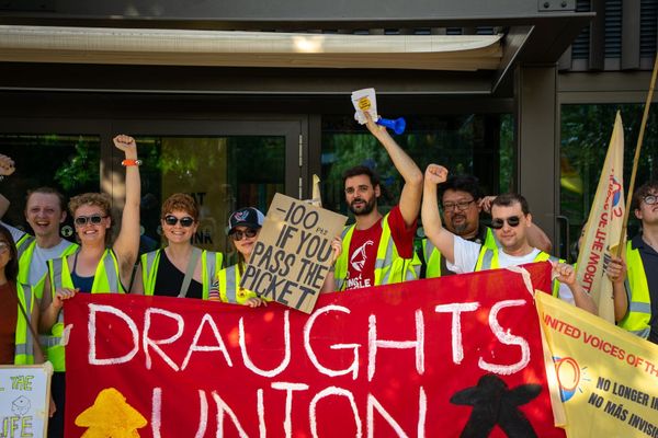 Draughts cafe workers in hi-vis vests holding protest signs in red and yellow.
