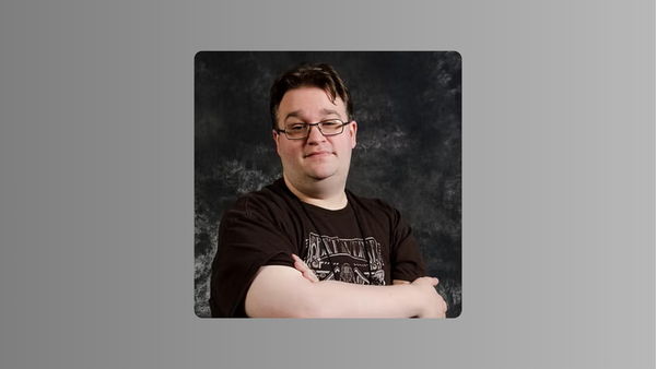 Photo of Rob Wieland from the chest up, his arms crossed on a grey and black background.