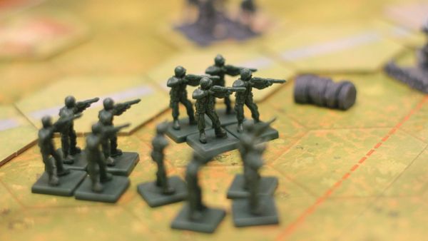 Twelve grey toy soldiers on a hexagon map, weapons raised at eye level. Other minis in the top right are out of focus.