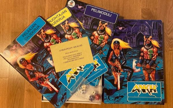 Four softcover RPG books and dice for a Finnish tabletop game called ANKH. Two blond adventurers in leather armor and weapons of a 1980s pulp style against a dark, gothic background.