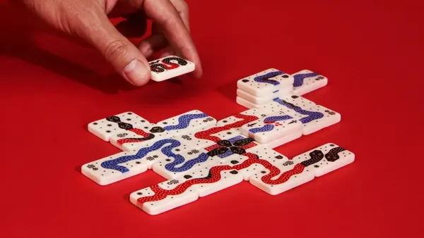 White game tiles featuring red, blue, and black snake illustrations on a red background. A hand reaches down from the top-left to place a tile.