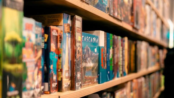 Wooden shelf full of board games in a brightly lit room. Only one, Cascadia, has its title legible.