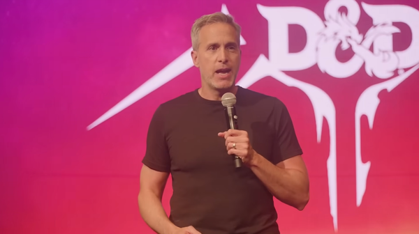 A man in a black shirt holding a microphone stands in front of a pink and purple screen with the D&D logo on it in white.