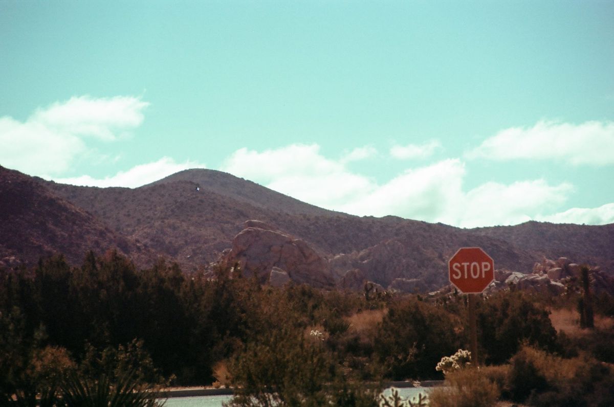 A crystal blue sky with scattered clouds above a mountain and a road with a stop sign.