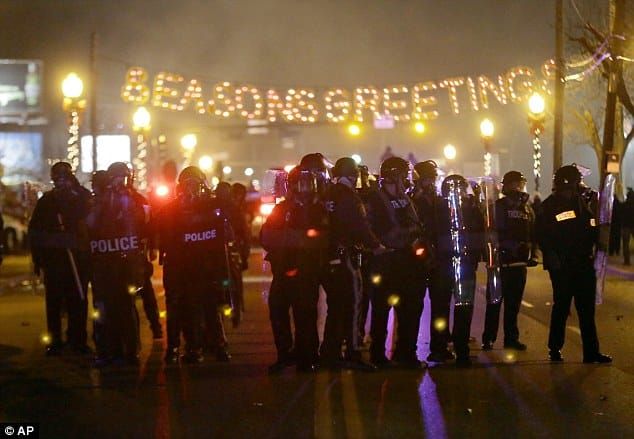 Riot cops in Ferguson, MO in 2014 assembled under a "Season's Greetings" lighted display that stretches across the street