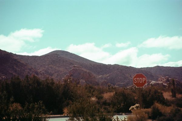 A crystal blue sky with scattered clouds above a mountain and a road with a stop sign.