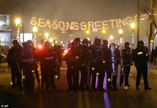 Riot cops in Ferguson, MO in 2014 assembled under a "Season's Greetings" lighted display that stretches across the street