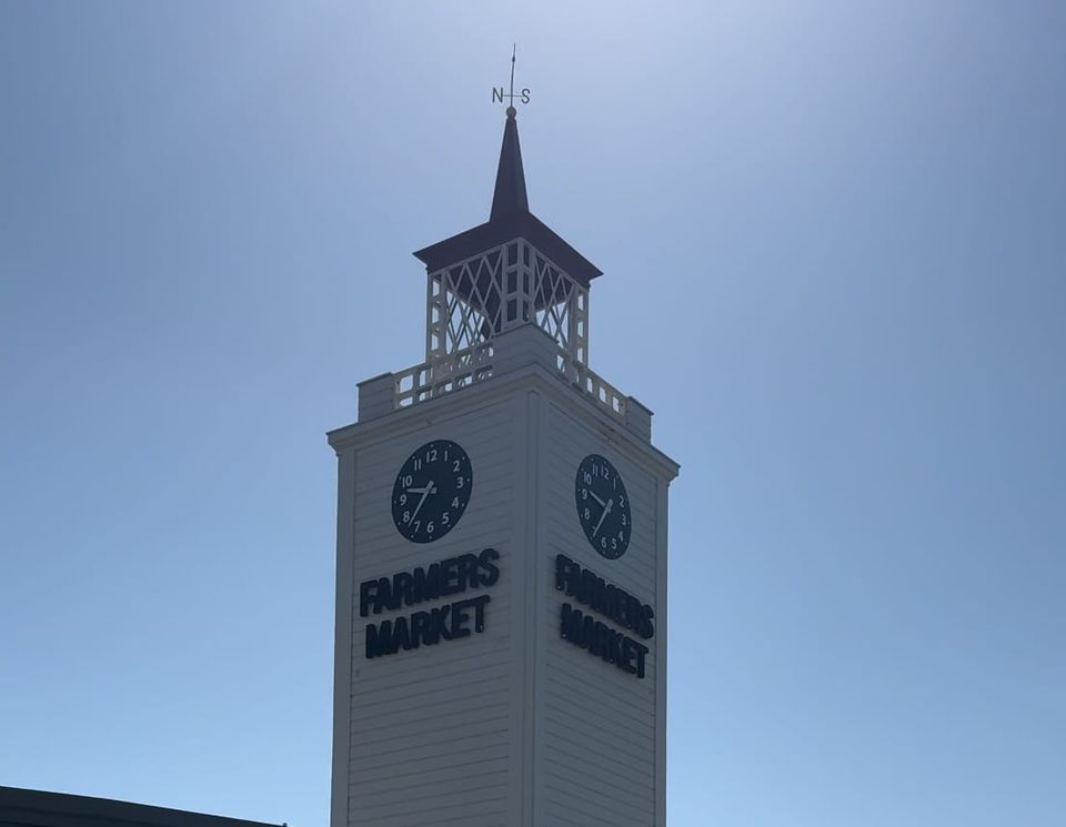 Tall clock tower of the historic Los Angeles Farmers Market on a sunny morning, casting a shadow on the pavement.
