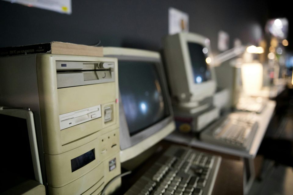 A row of vintage beige desktop computers and CRT monitors, reminiscent of 1990s tech setups.