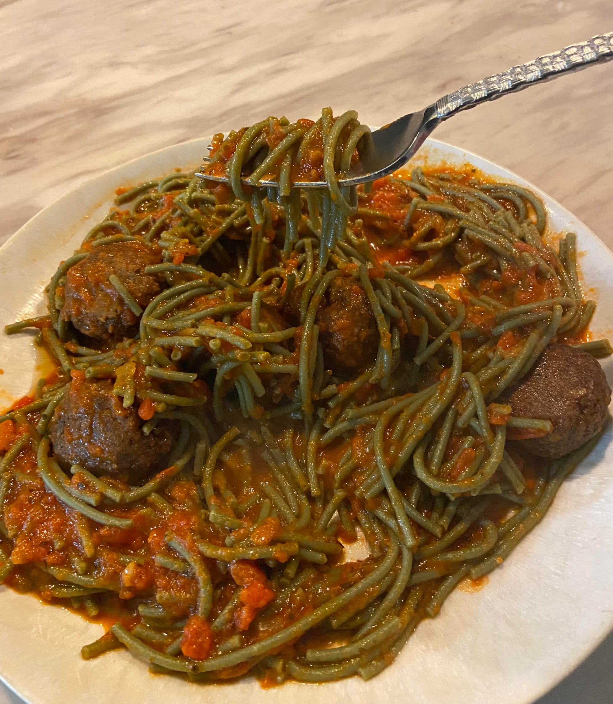 A plate of green pasta with tomato sauce and meatballs
