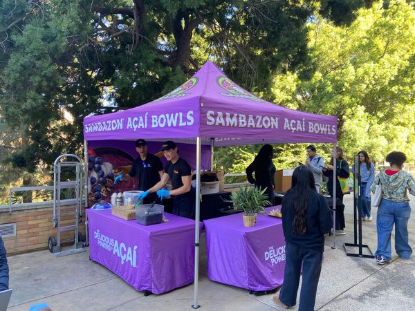 A Sambazon-branded outdoor pop-up tent with workers serving açaí bowl samples to students.